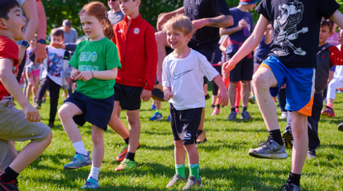 A photo of a gathering of people, mainly young children, warming up before starting a park run. Everyone is in fitness clothing.