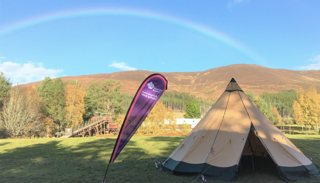 A pop-up teepee tent set up in an outdoor location with trees and hills in the background. Beside the tent is a banner for Alzheimer Scotland.