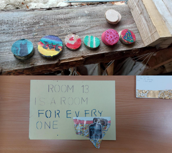 Image shows 6 colourful wooden cookies on a wooden bench and below there is an image of a piece of paper that says, 'room 13 is a room for everyone'